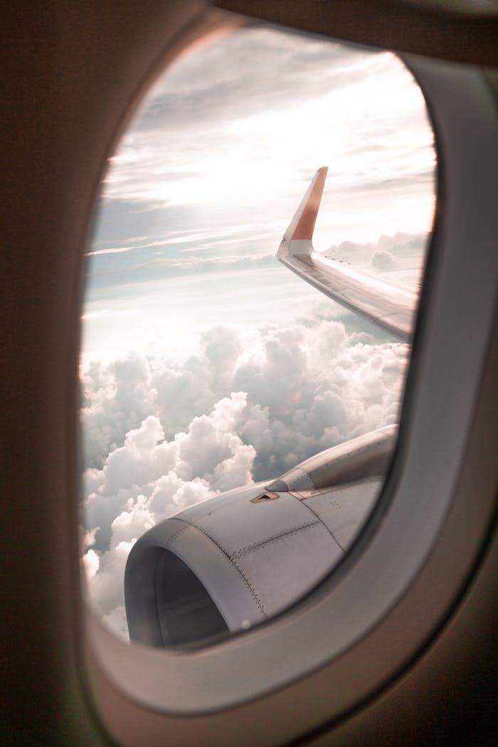 View of clouds and airplane wing from a window seat, depicting a serene flying experience.